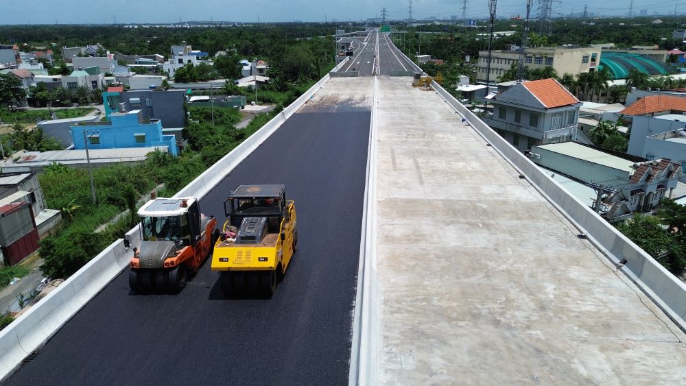 Tại công trường, phần đầu cầu kết nối đoạn dẫn cao tốc đang được các công nhân thảm nhựa.